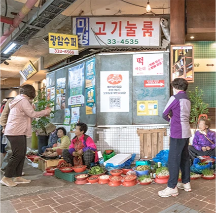 좌판에 채소를 펼쳐 놓고 앉은 상인들과 오래된 간판이 어우러진 정겨운 시장 골목 풍경