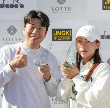엄지를 든 남성과 흰 모자를 쓴 여성이 크리스털 트로피를 들고 환하게 웃는 시상 장면
