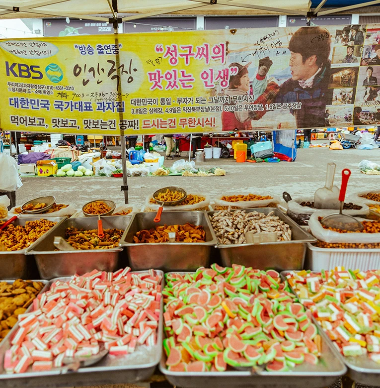KBS 방송 출연 현수막이 걸린 두리제과 좌판에 색색의 젤리와 과자를 통에 가득 담아 진열해 놓은 모습