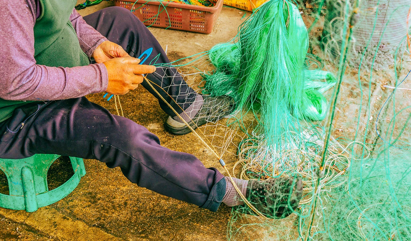 초록색 그물을 무릎에 놓고 가위로 손질하는 어민의 모습