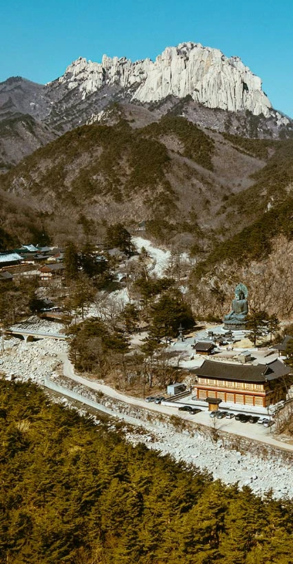 눈 덮인 설악산 울산바위 아래 골짜기에 단청 건물이 자리한 신흥사를 높은 곳에서 내려다본 전경