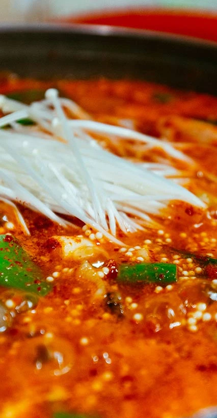 붉고 칼칼한 국물 위에 흰 팽이버섯과 푸른 고추를 올려 끓이는 도치알탕 클로즈업