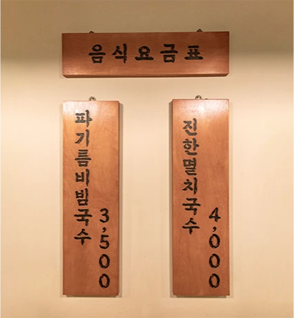 파기름비빔국수와 진한멸치국수 가격을 적어 걸어 둔 나무 음식요금표