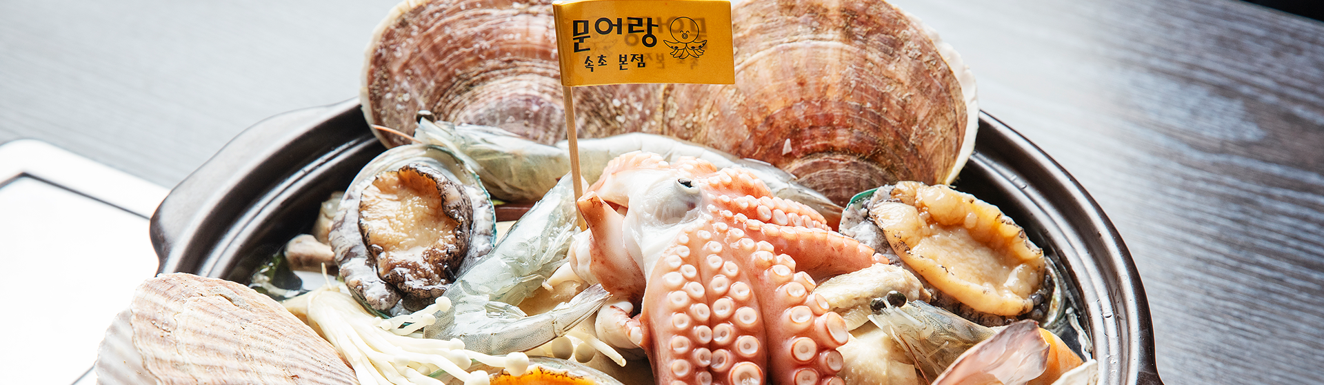 큼직한 가리비와 전복, 문어, 표고버섯 등 해산물이 가득 담긴 해물전골 냄비와 문어랑이라 적힌 노란 이름표