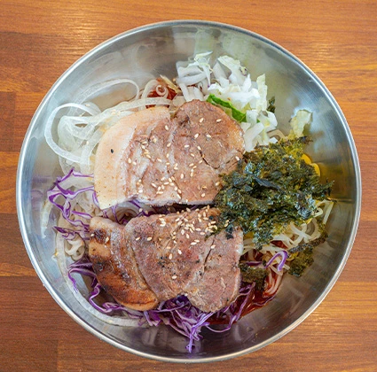 양념 채소 위에 돼지고기 수육과 김을 올린 비빔국수를 위에서 내려다본 모습
