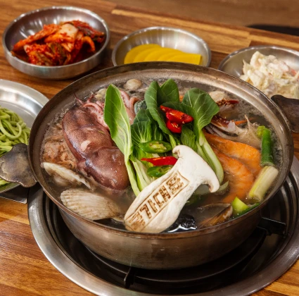 통오징어와 조개, 채소가 가득 담긴 해물칼국수 전골과 곁들이 반찬이 차려진 상