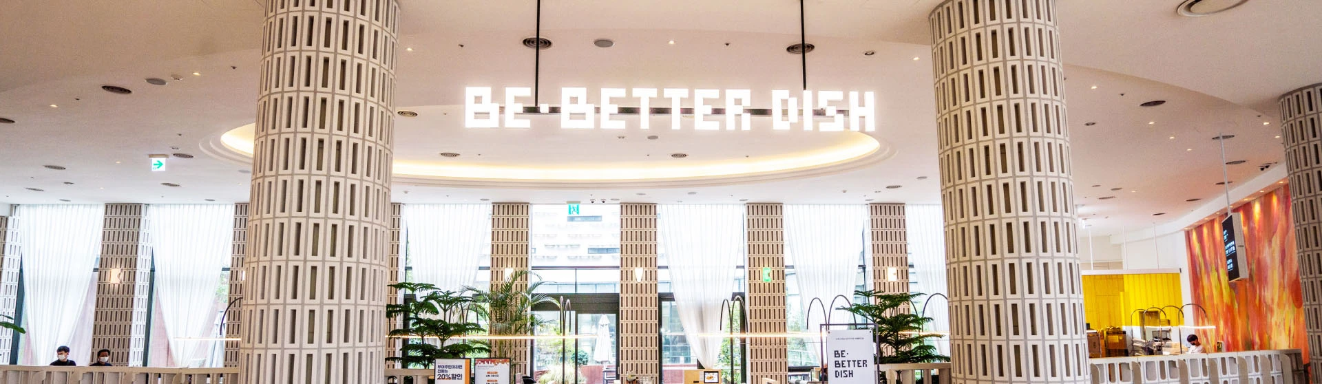 롯데리조트부여 1층 로비에 자리한 브런치 카페 비베러디쉬, 흰 기둥들과 천장의 BE BETTER DISH 사인이 보이는 밝은 내부