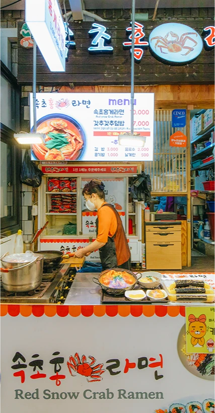 홍게라면 간판과 메뉴판 아래에서 마스크를 쓰고 음식을 조리하는 가게 주인의 모습
