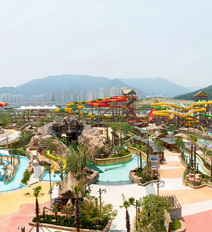 산과 도시를 배경으로 알록달록한 워터슬라이드와 유수풀이 넓게 펼쳐진 롯데워터파크 김해 야외 전경