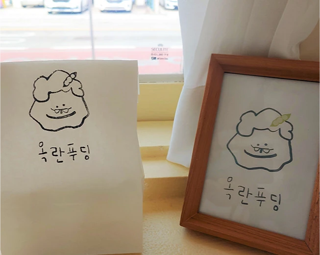 창가에 푸딩 캐릭터를 그린 종이와 액자를 나란히 세워둔 최옥란 순두부의 옥란푸딩 안내