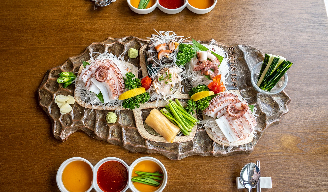 제주도 모양 돌 접시에 돌문어 숙회와 전복, 뿔소라회, 채소를 푸짐하게 담아 위에서 내려다본 해산물 한 상