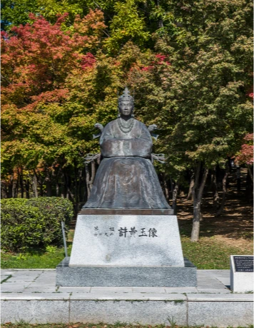 단풍 든 나무를 배경으로 돌 받침대 위에 세워진 허왕후 좌상 동상