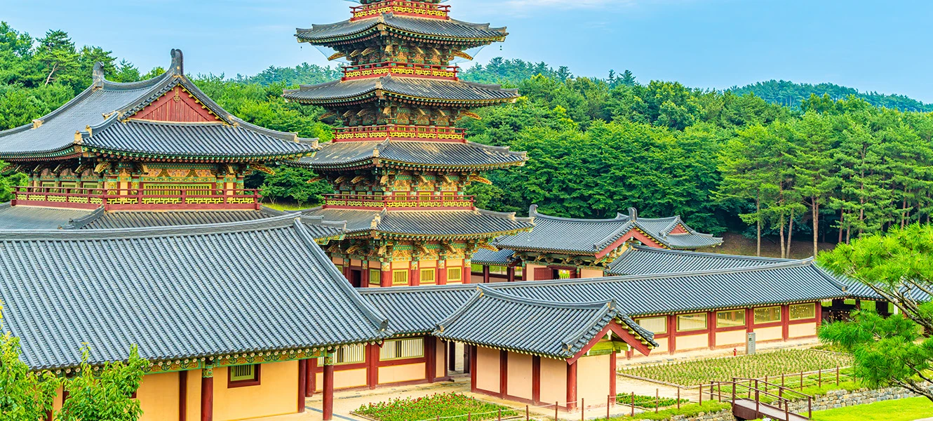 푸른 산을 배경으로 백제문화단지의 단청 기와 전각과 오층 목탑이 어우러진 한낮 전경