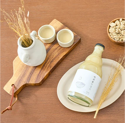 원목 도마 위 백자 주전자와 잔, 접시에 놓인 이시보 오리지널 막걸리 병