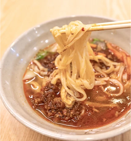 붉은 마라 국물 위로 젓가락으로 면을 집어 올린 마라칼국수