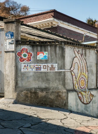 실래골 마을 시멘트 담벼락에 꽃 모자이크와 한글 마을 이름, 커다란 손 모양 모자이크가 새겨진 벽화마을 입구