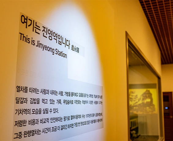 여기는 진영역입니다라는 안내 문구가 적힌 노란 조명의 전시 벽면