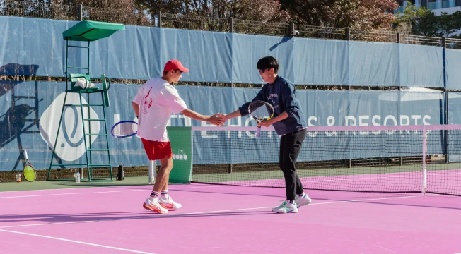 분홍 코트 네트를 사이에 두고 두 남성 선수가 경기를 마치고 악수하는 장면, 옆에 심판석