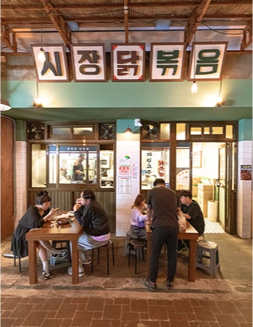 시장닭볶음이라 적힌 레트로 간판 아래 야외 테이블에서 식사하는 손님들