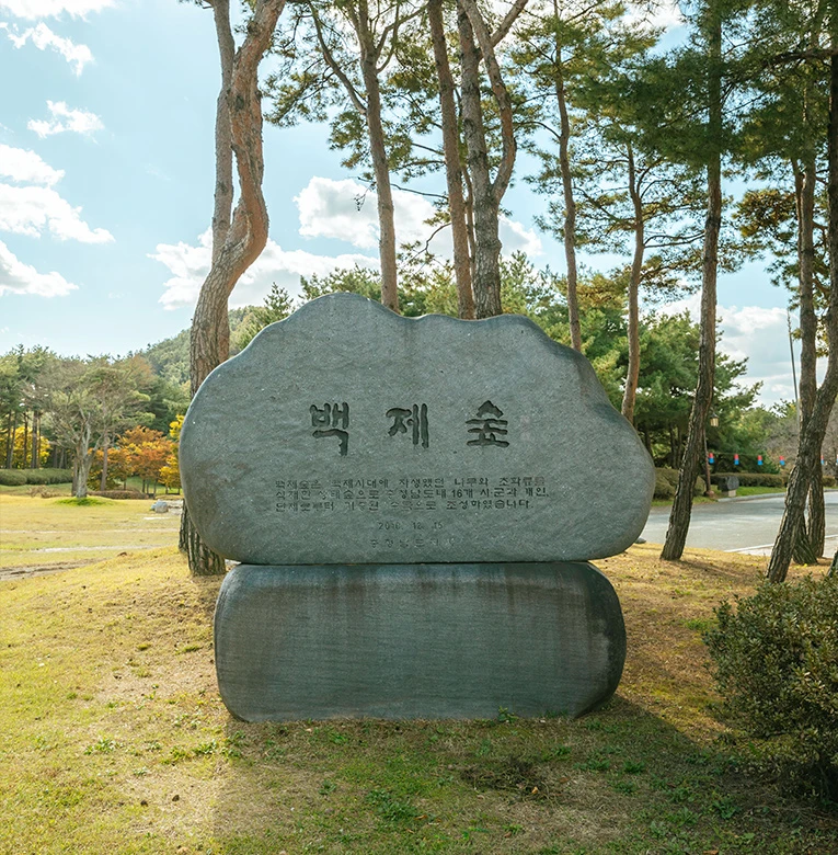 백제숲이라 새겨진 둥근 표석이 소나무 숲을 배경으로 잔디밭에 놓여 있는 모습