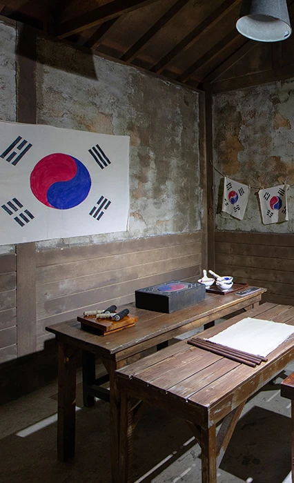 태극기와 작은 태극기들이 걸린 낡은 흙벽 방, 나무 탁자 위에 옛 소품이 놓인 경성편 세트