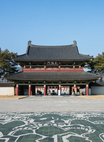 단청을 입힌 웅장한 기와 누각 형태의 정문이 너른 돌바닥 마당 너머로 우뚝 서 있는 백제문화단지 입구 모습