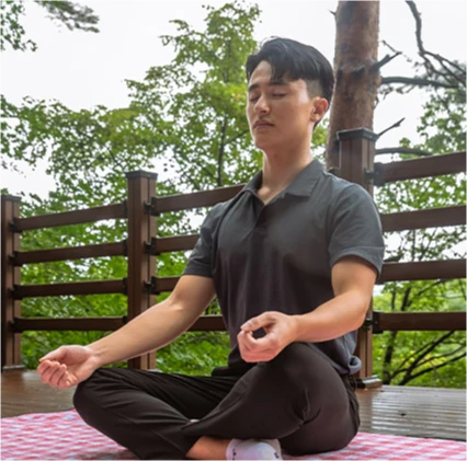 데크 위에서 눈을 감고 가부좌로 앉아 명상에 잠긴 젊은 남성의 모습