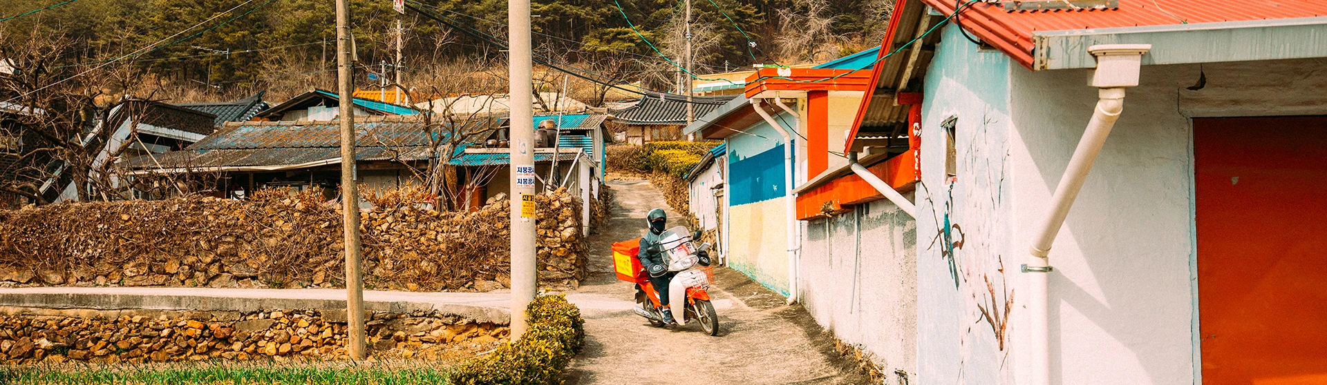 알록달록 벽화로 꾸며진 시골 마을 골목, 좁은 길에 오토바이가 세워져 있고 돌담과 주황 지붕 집들이 이어진 풍경