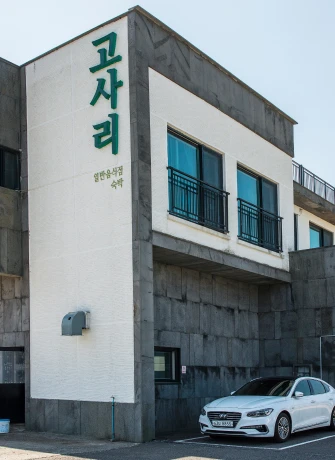 회색 돌 외벽 건물 한쪽에 고사리라고 세로로 적힌 간판이 걸리고 앞에 흰 승용차가 주차된 식당 외관
