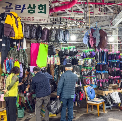 가방과 옷가지가 빼곡히 걸린 만물 잡화점에서 물건을 고르는 손님들