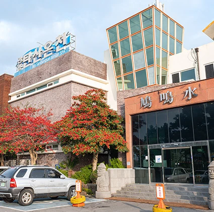 주차장 너머로 보이는 산방산 탄산온천 건물 외관과 가을빛으로 물든 나무들