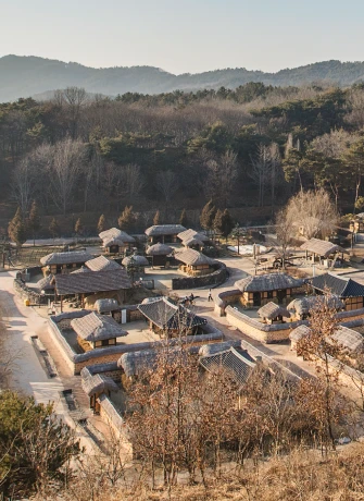 겨울빛 산자락을 배경으로 초가집들이 모여 있는 생활문화마을을 언덕 위에서 내려다본 전경