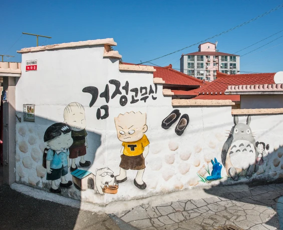 흰 담벼락에 검정 고무신 글씨와 만화 캐릭터들, 이웃집 토토로까지 그려진 레트로 감성의 벽화마을 골목