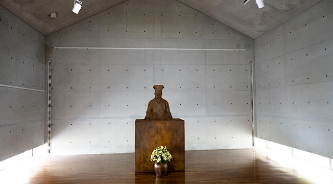 텅 빈 노출 콘크리트 공간 가운데 추사 김정희 좌상과 꽃을 꽂은 항아리가 놓인 추사관 내부