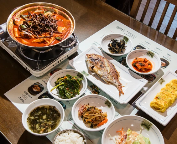 고사리 갈치조림 전골과 구운 생선, 여러 가지 반찬과 밥이 한 상 가득 정갈하게 차려진 식당 상차림