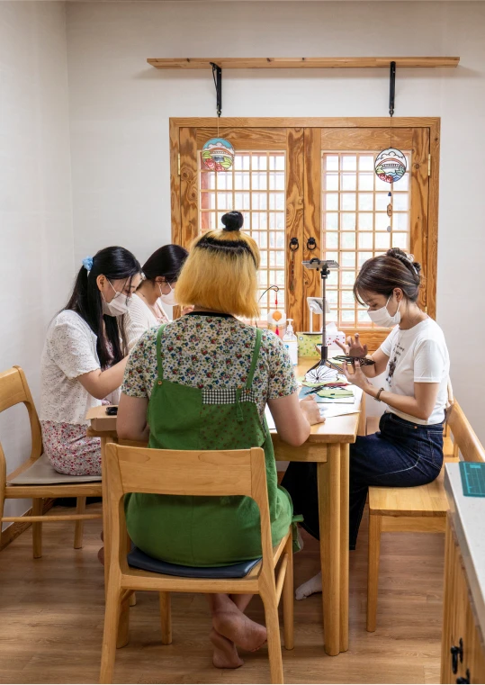 한옥 창이 있는 작업실에서 사람들이 테이블에 둘러앉아 한지 공예를 체험하는 모습