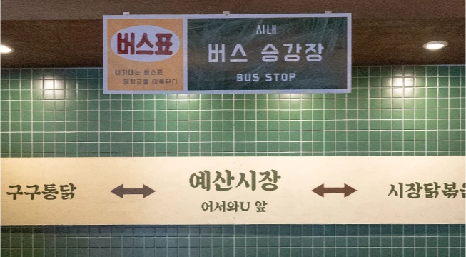버스 승강장을 흉내 낸 초록 타일 벽의 예산시장 방향 안내판