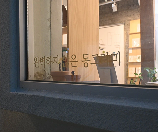 통창 유리에 '완벽하지 않은 동그라미'라는 문구가 새겨진 동그란 책방의 창가