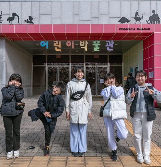 부여 어린이박물관 입구 앞에서 아이들이 익살스러운 포즈로 단체 기념사진을 찍는 모습