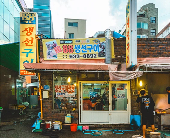 노란 차양에 88생선구이 상호와 전화번호가 적힌 골목 안 생선구이 식당 외관