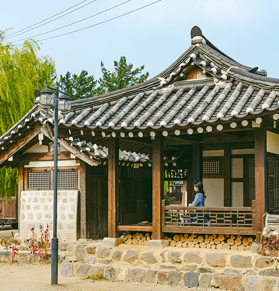 기와지붕 한옥 누마루에 한 사람이 앉아 있는 고즈넉한 선샤인 스튜디오 풍경