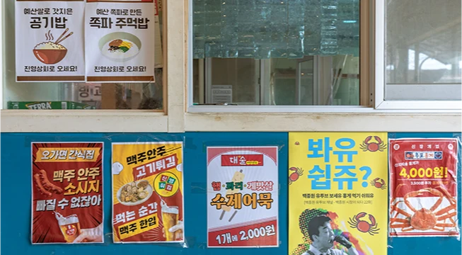 공깃밥과 주먹밥 안내문이 붙은 창문 아래 색색의 음식 홍보 포스터가 줄지어 붙은 벽면