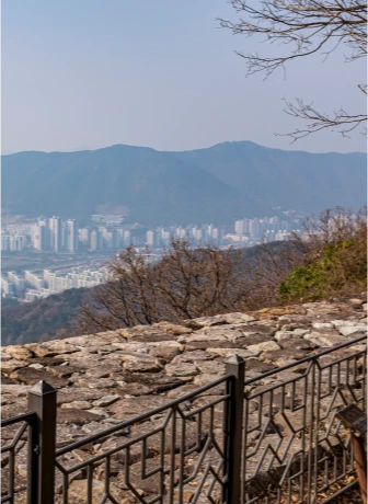 분성산성 돌담과 난간 너머로 멀리 산과 김해 시내가 내려다보이는 전망