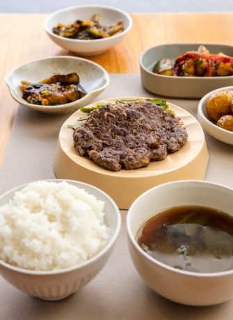 사계반상의 정갈한 한식 반상 차림. 가운데 나무 접시에 노릇하게 구운 고기 요리가 놓이고 흰쌀밥과 맑은 장국, 색색의 밑반찬이 함께 차려져 있다.
