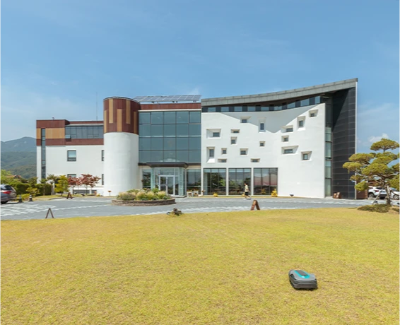 산자락을 배경으로 한 설악산책 건물 외관, 흰색 3층 건물 앞 잔디밭에 로봇 잔디깎이가 놓여 있다
