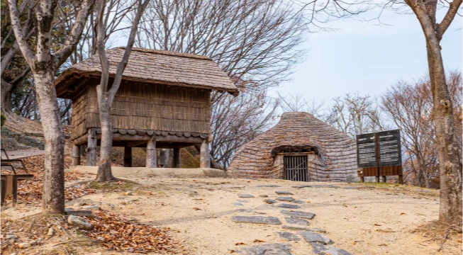 봉황동유적에 복원된 고상가옥과 움집, 흙길과 낙엽이 깔린 야외 풍경