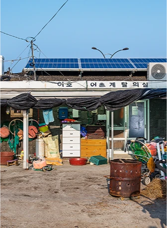 태양광 패널을 얹은 어촌계 탈의실 건물과 그 앞에 널린 그물과 작업 도구들
