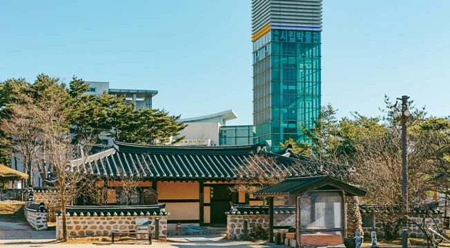 유리 전망탑을 배경으로 돌담을 두른 기와 한옥이 자리한 속초시립박물관