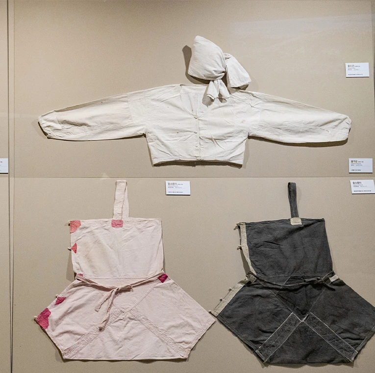 무명천으로 지은 흰 적삼과 분홍빛, 회색 물소중이를 벽면에 나란히 전시한 모습