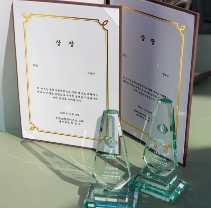 펼쳐진 상장 두 장과 그 앞에 놓인 크리스털 트로피가 테이블 위에 진열된 모습